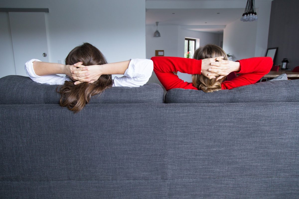Two women seen from behind relaxing on a gray sofa