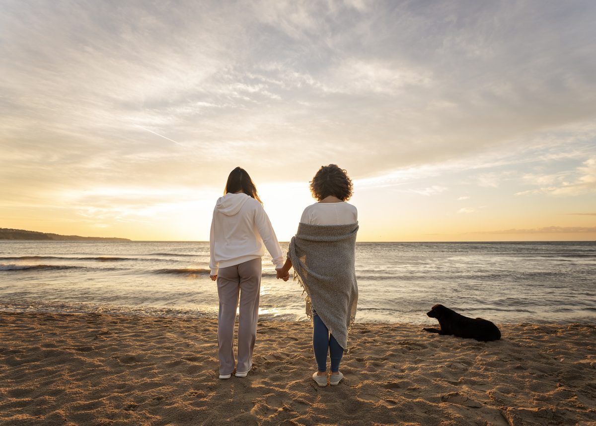 Two women seen from behind walking hand in hand on a beach at sunset