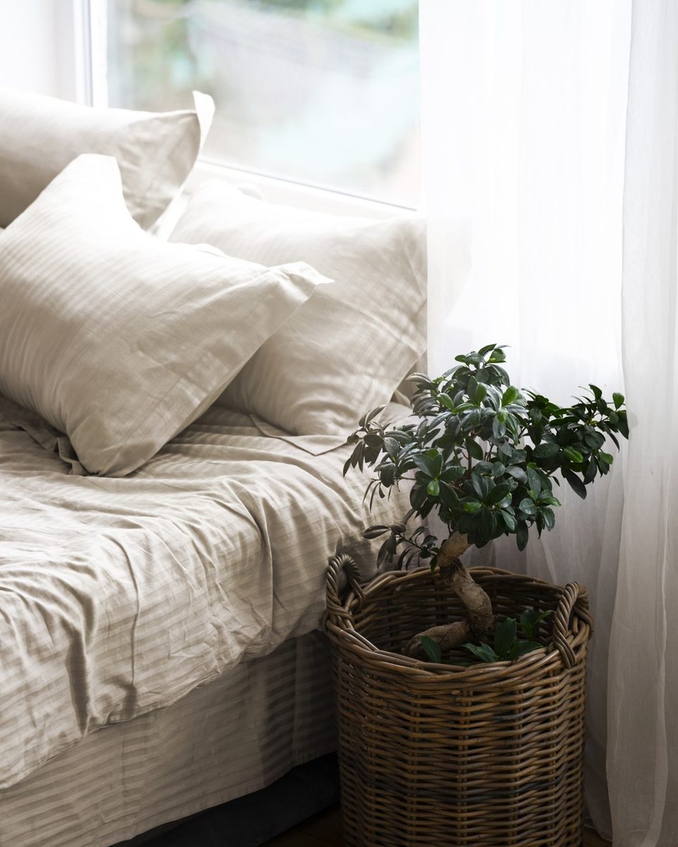 Small bright bedroom with a cream linen bed, white walls, a wooden nightstand and soft daylight from a window