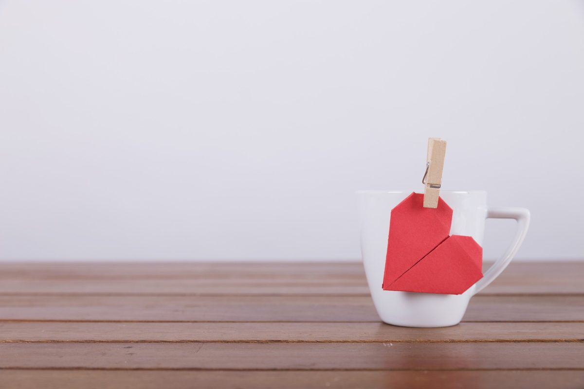 Red paper heart clipped to a white mug on a wooden table