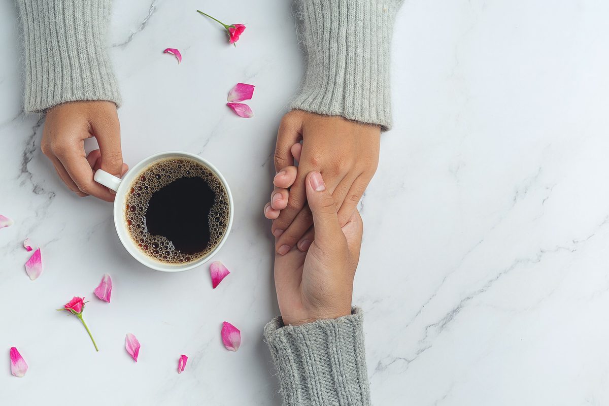 Two hands holding each other next to a cup of coffee on a white marble table