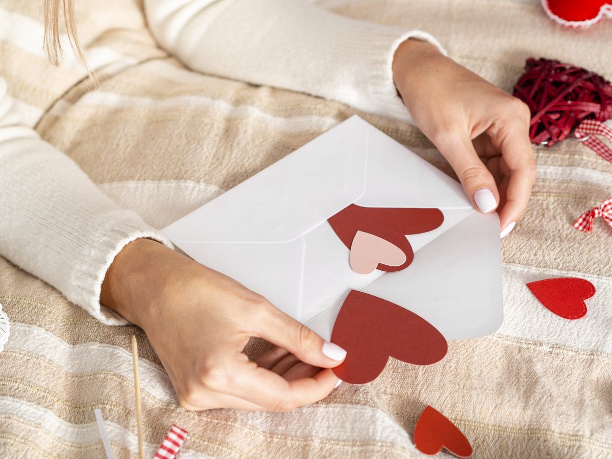 Woman's hands opening an envelope with paper hearts on a cozy blanket