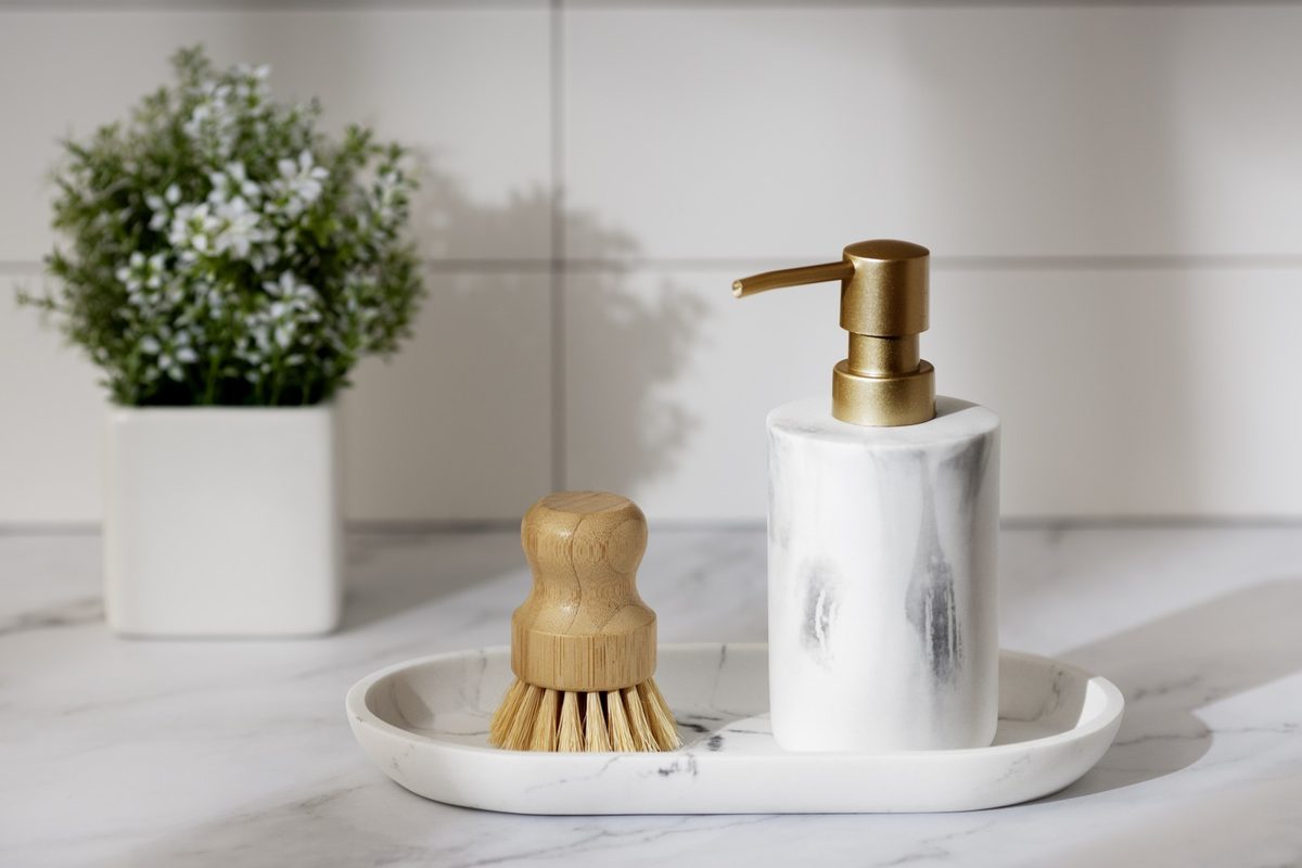 Rolled white towels, a glass soap dispenser and a small woven basket in a bright minimal bathroom