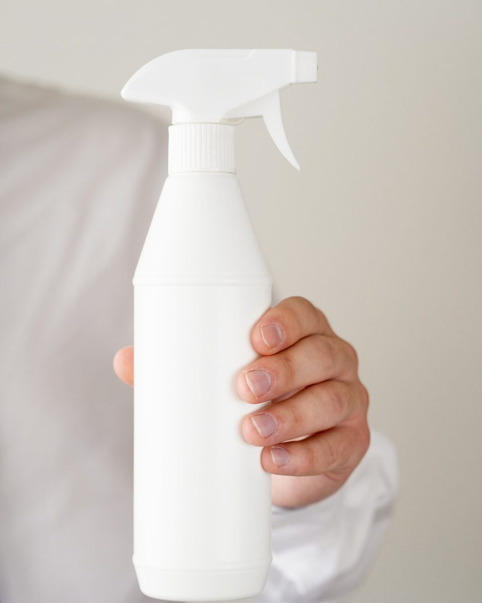 Woman's hands placing a white spray bottle into a clear storage bin on a light countertop