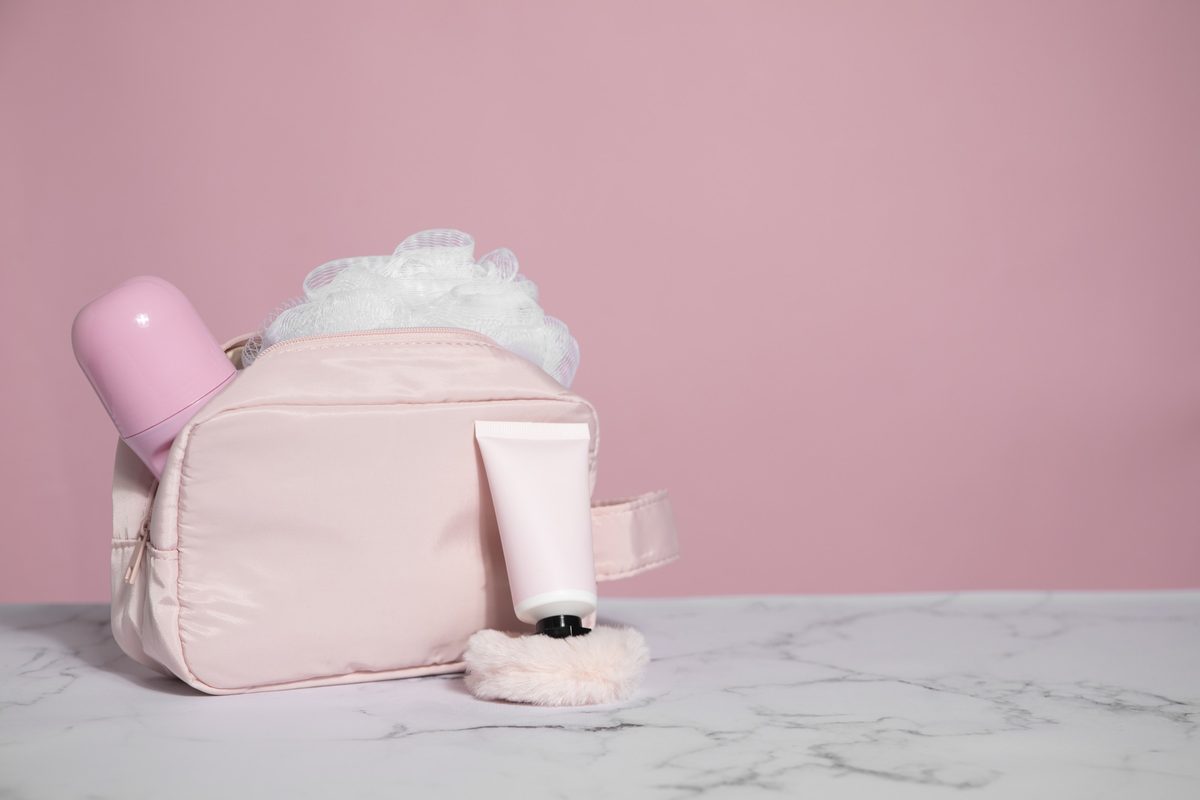 Pink makeup bag with a pink bottle and cosmetics on a white table