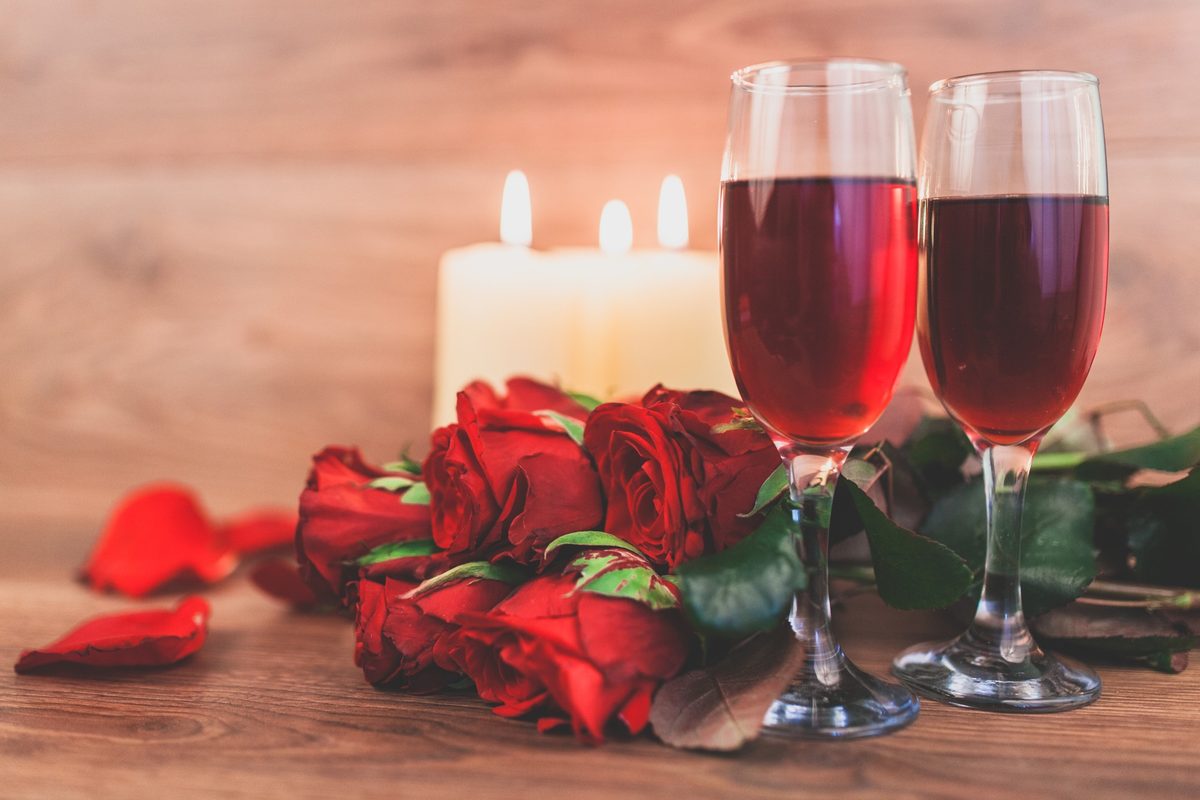 Two glasses of red wine with candles and red roses on a wooden table