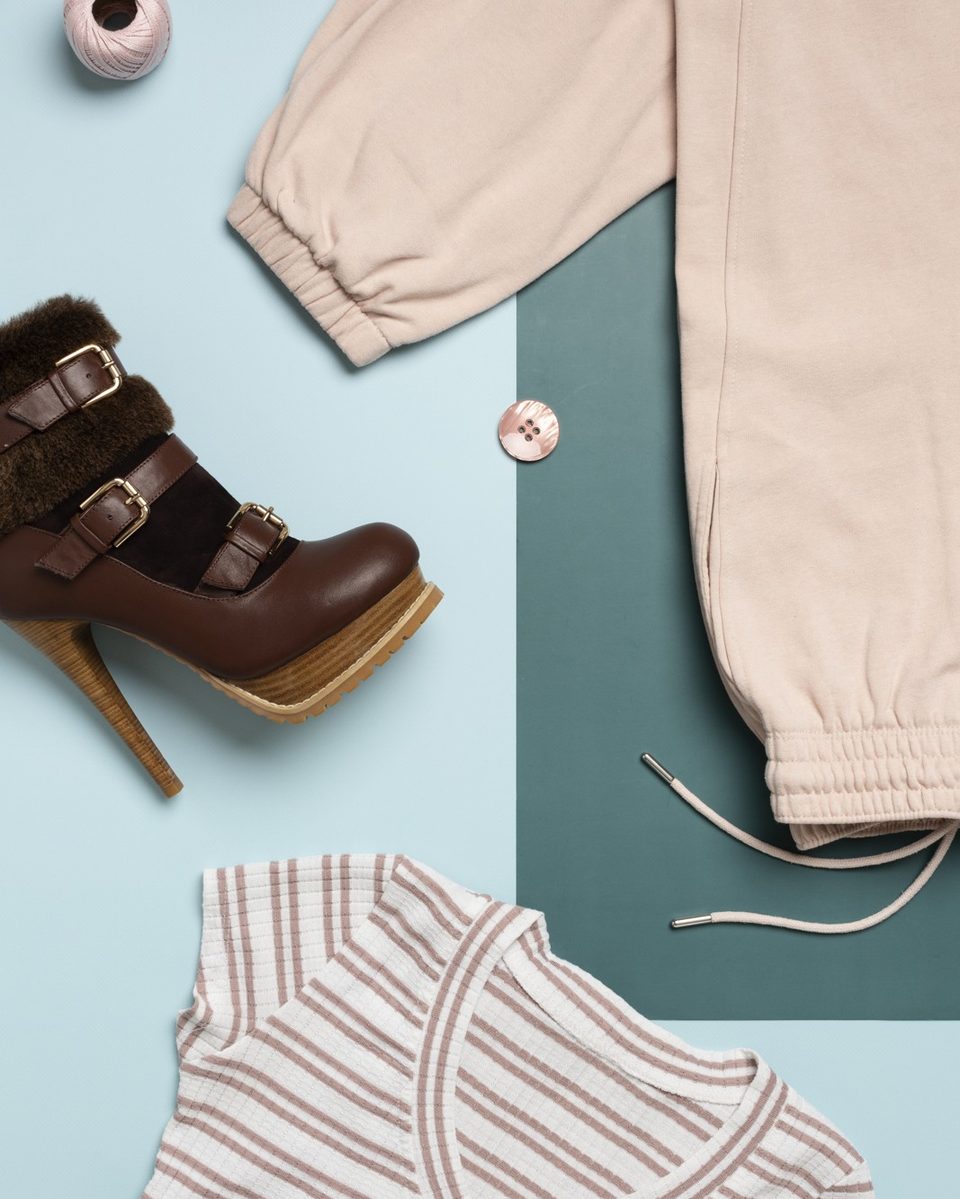 Women's weekend outfit pieces laid on a bed with a beige trench coat, pastel silk scarf and white leather sneakers